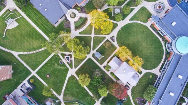 Aerial view of a university or college campus with winding pathways, green lawns, and various buildings.